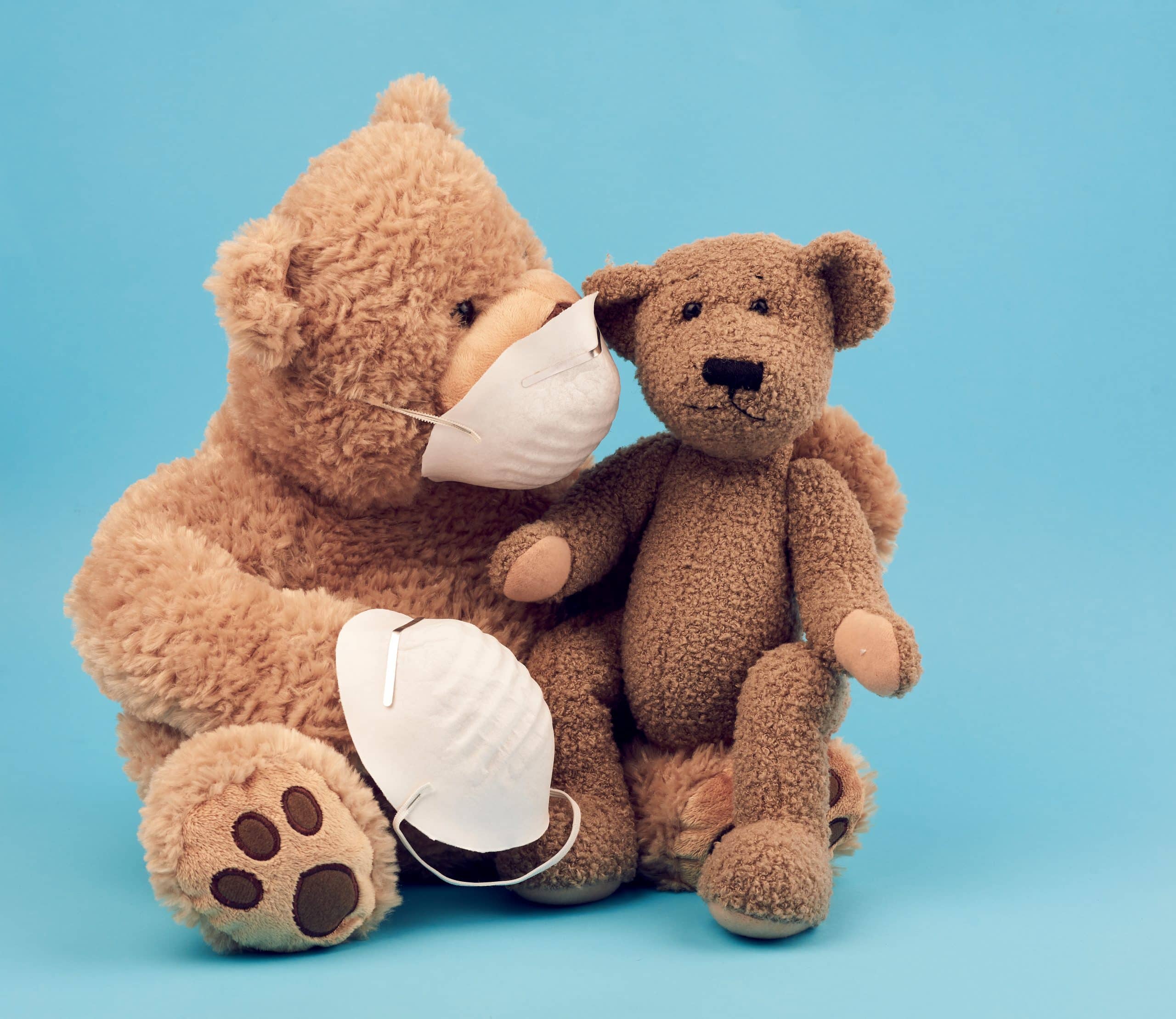 large teddy bear in a white mask transfers the accessory to another, concern for the health of those who are exposing, toys on a blue background